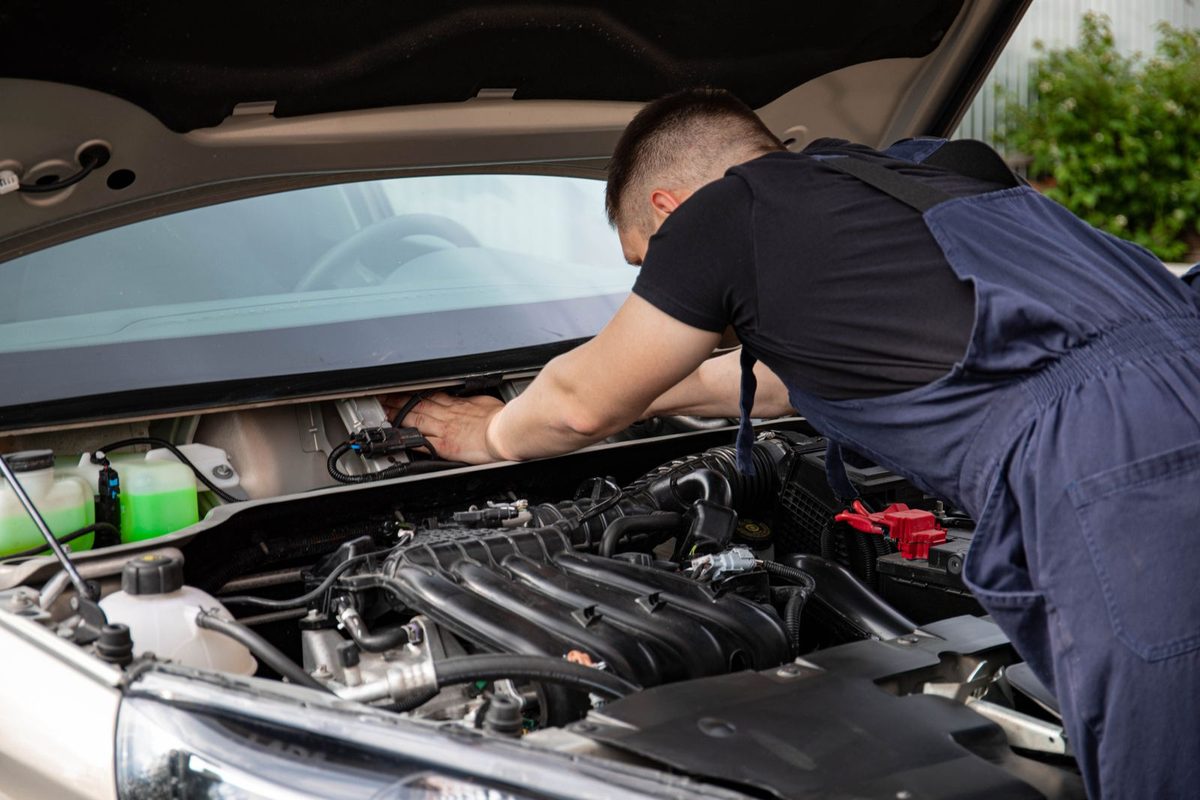 Mechanic checking the engine under the bonnet of a car in a garage