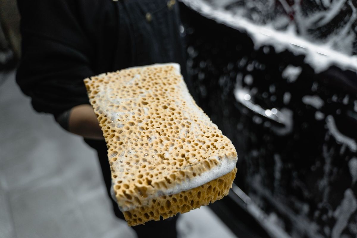 A soapy sponge being used to wash a car panel