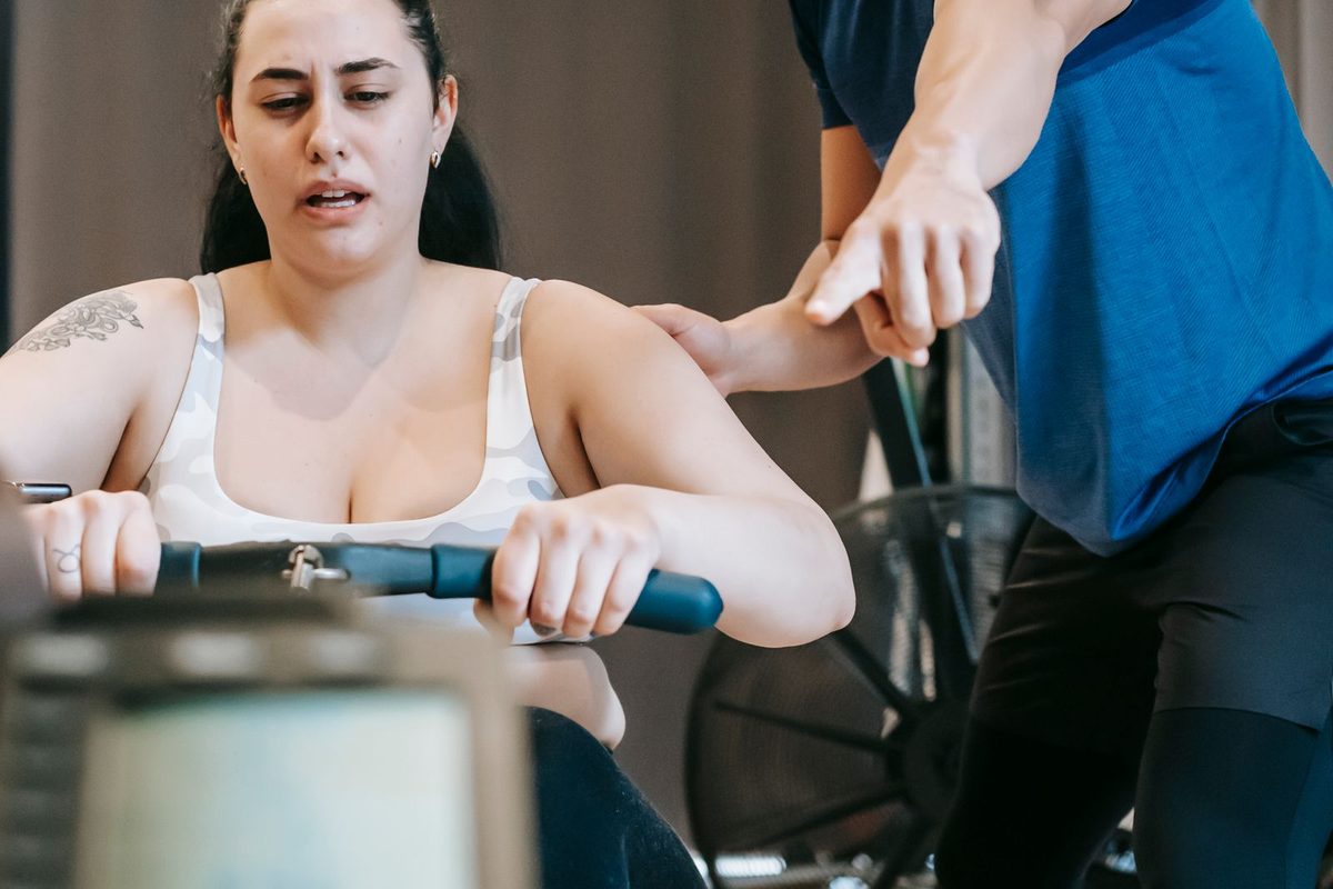 Trainer helping a member on a rowing machine in a friendly gym