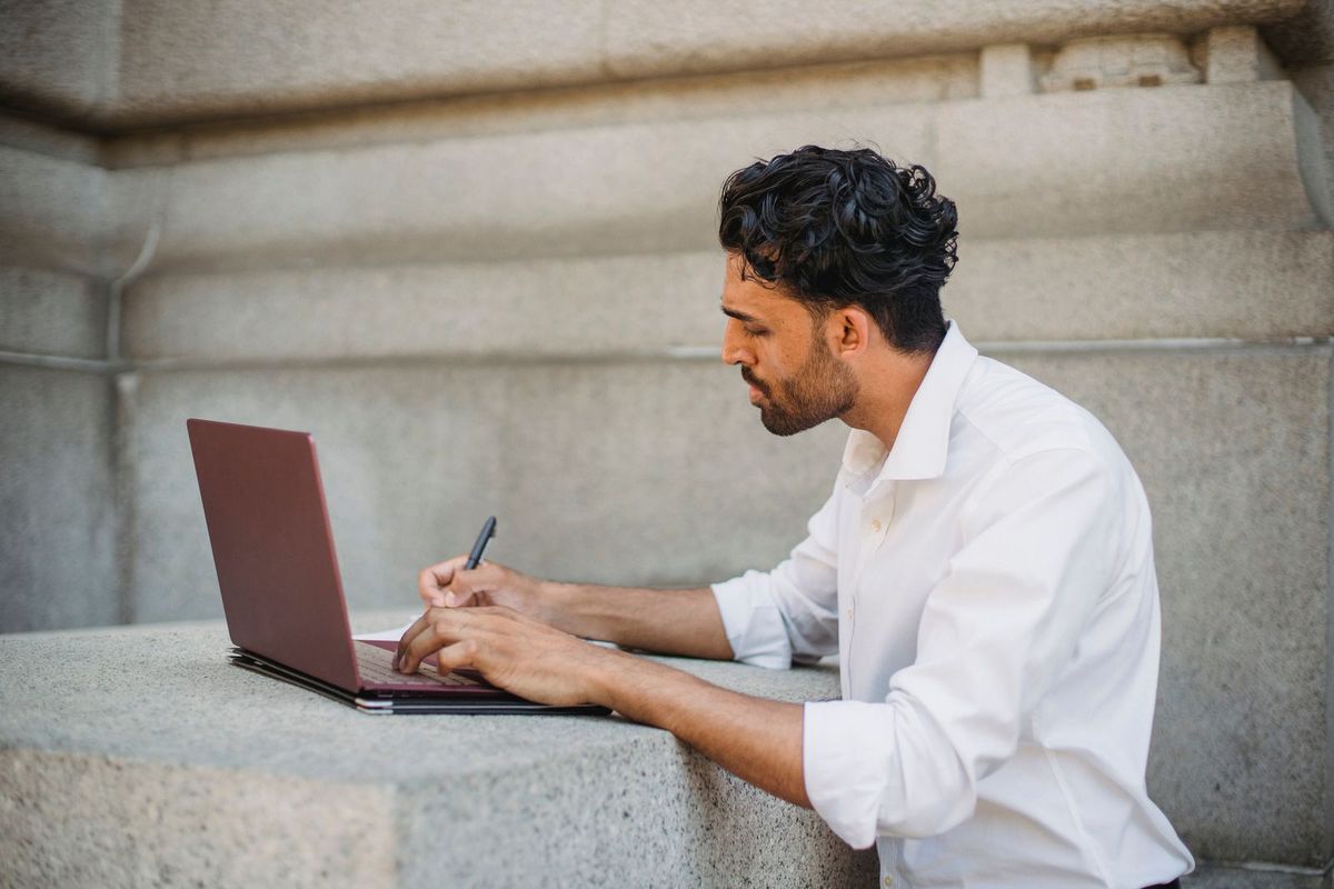 Person doing research on a laptop with a notebook