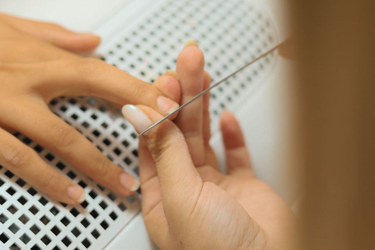 Nail technician shaping a client's nails at a salon station