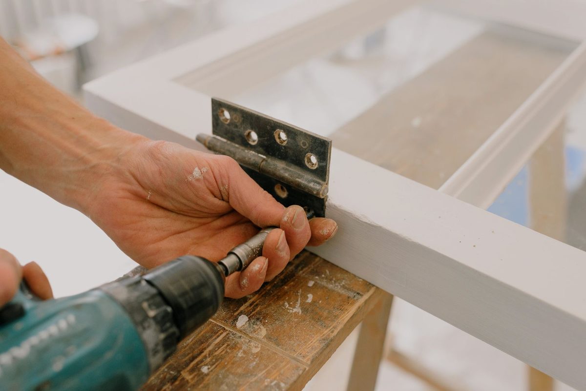 Handyman drilling a hinge while fitting a door in a home