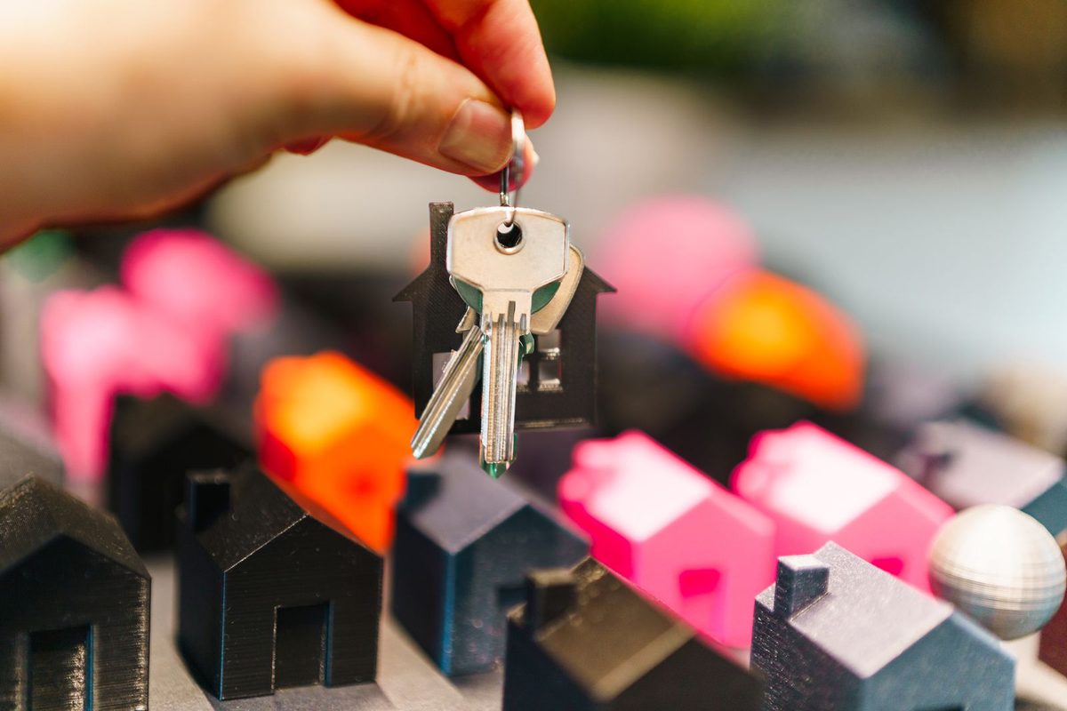 Hand holding house keys above small model homes