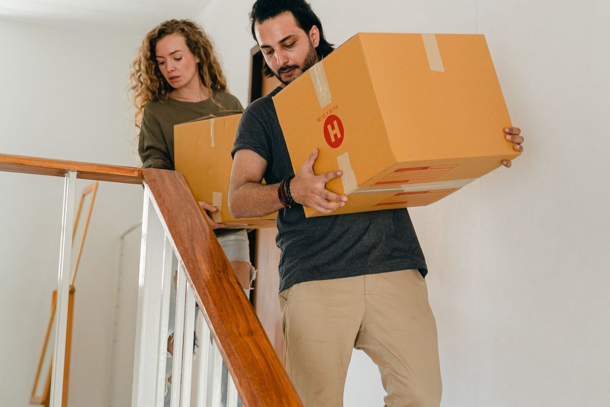 Couple carrying moving boxes down the stairs on moving day