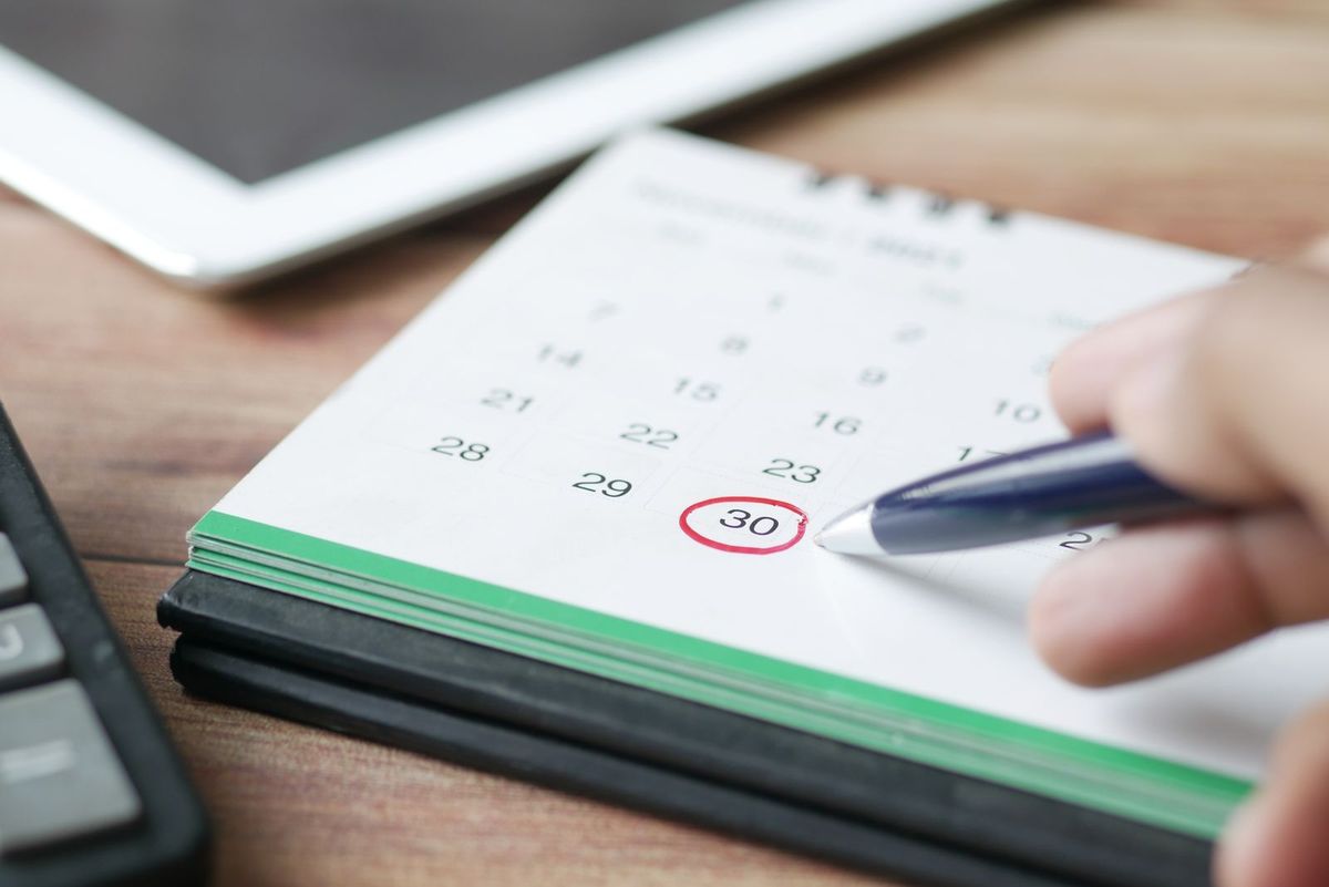 Hand circling a date on a calendar with a pen