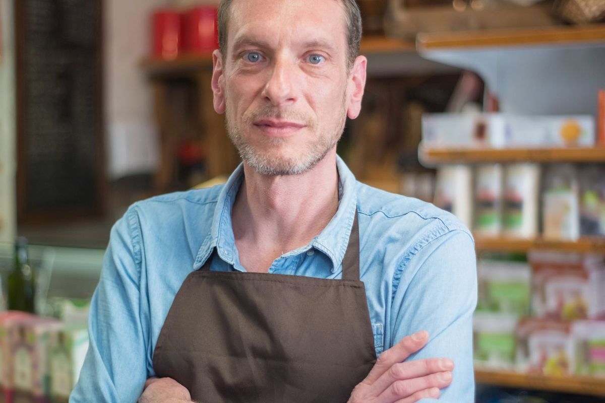 A shop owner in an apron standing in their store