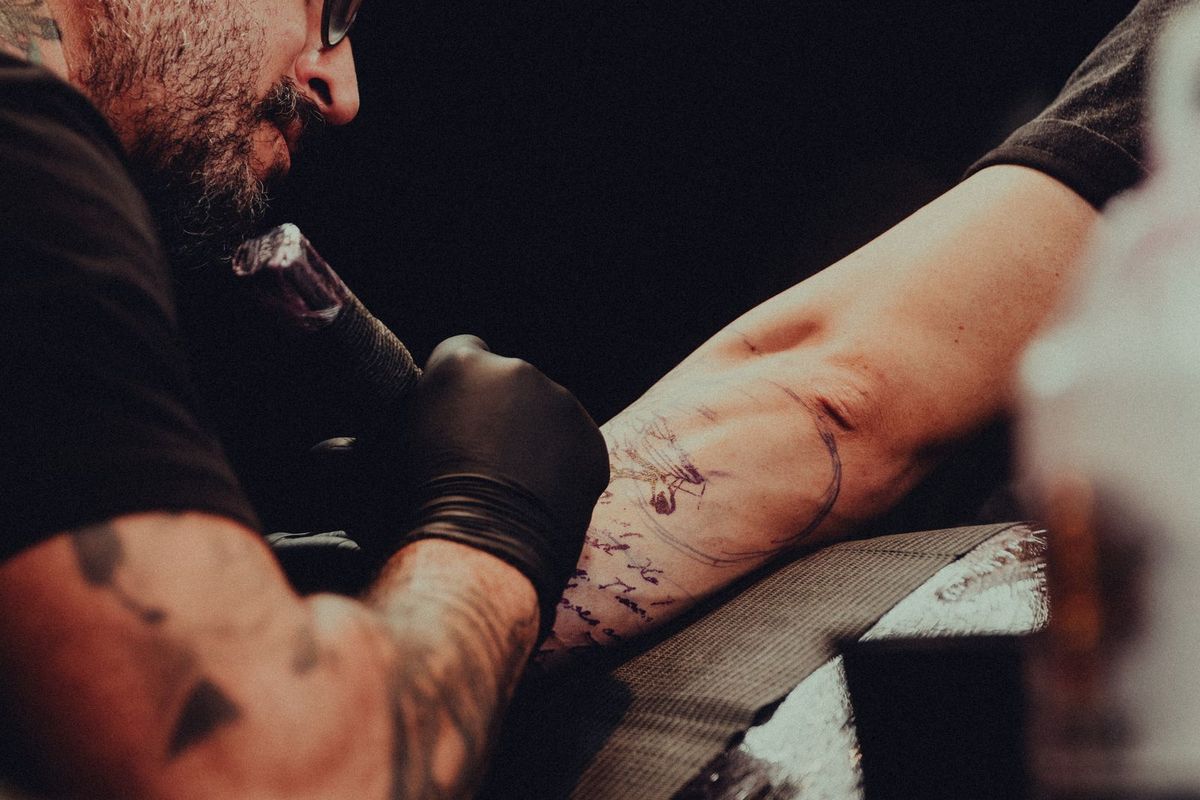 A tattoo artist working on a client in a studio