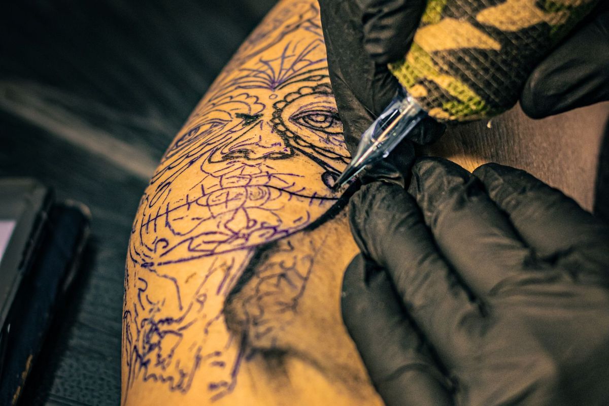Gloved hands using a tattoo machine on skin
