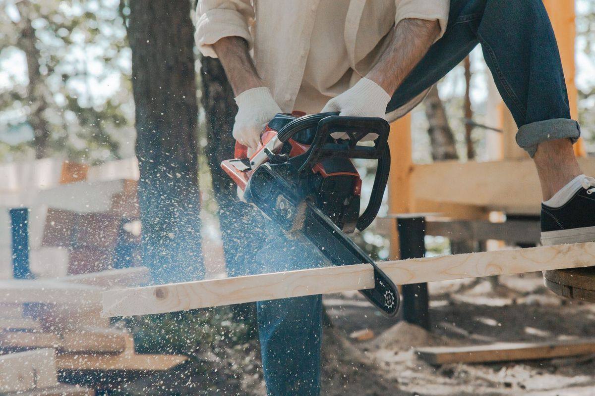 A person using a chainsaw with protective gear and flying sawdust